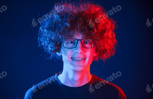 Preview: Portrait of young man with curly hair that is standing indoors, illuminated by neon lighting