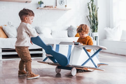 Preview: Two little boys in retro pilot uniform having fun with toy plane indoors