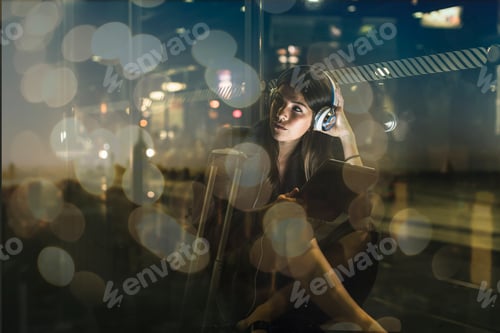 Preview: Young woman with tablet and headphones sitting outdoors at night