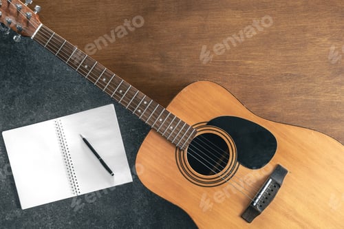 Preview: Acoustic guitar and notebook on a textured black and wooden background.