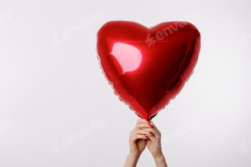 Preview: A hand holding a shiny red heart-shaped balloon against a clean white background, symbolizing love