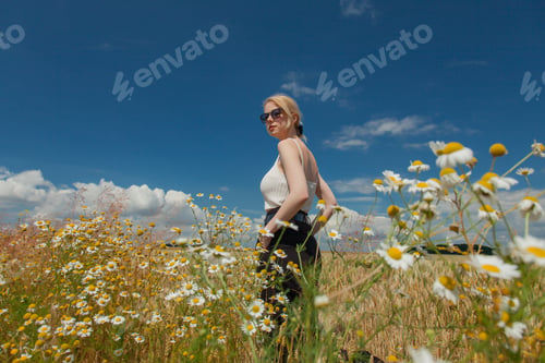 Preview: Stylish woman with blond hair posing in formal clothes on chamomile meadow