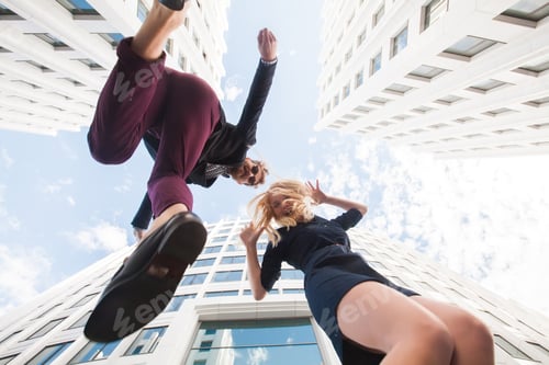 Preview: Cheerful young couple fooling around, jumping on the background of the building. Bottom view