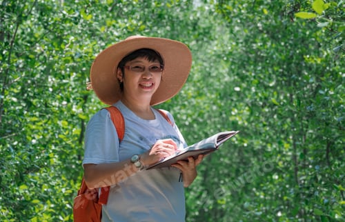 Preview: Portrait of female tourist smiling and looking at camera while taking notes in natural parkland