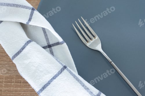 Preview: Close-up silver fork, empty gray plate and white textile napkin on wooden table
