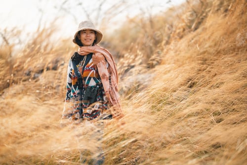 Preview: Woman traveler wearing colorful patterned sweater and hat standing in golden grass field