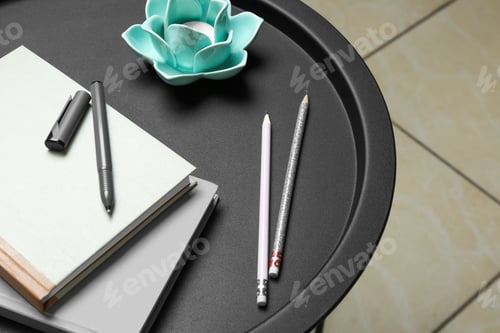 Preview: Notebooks, pen, pencils and decorative holder with candle on round table indoors, closeup