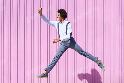 Preview: Black man taking a selfie with his smartphone while jumping outdoors