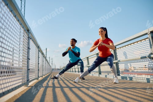 Preview: Happy athletic couple doing stretching exercises while working out outdoors.