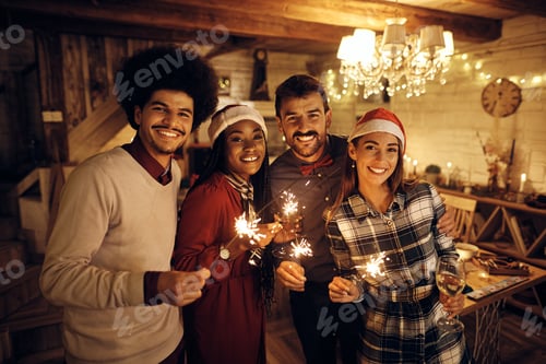 Preview: Happy people using sparklers and drinking wine while celebrating New Year and looking at camera.