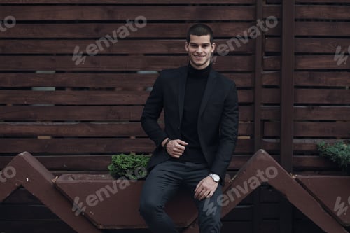 Preview: Fashionable man, wearing a suit, sitting against the wooden wall