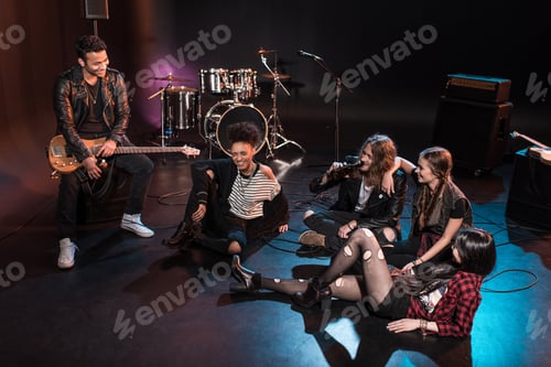 Preview: Young rock and roll band sitting together and drinking beer after concert on stage