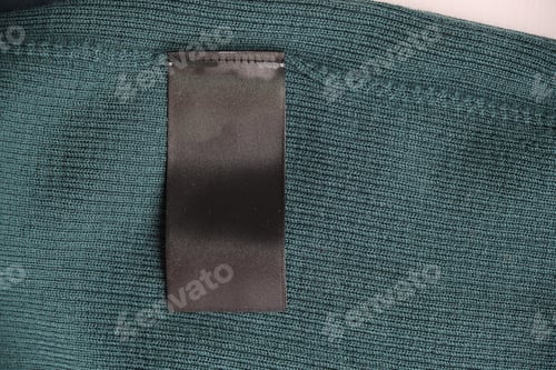 Preview: Blank black laundry care clothes label on green fabric texture background. natural merino wool.