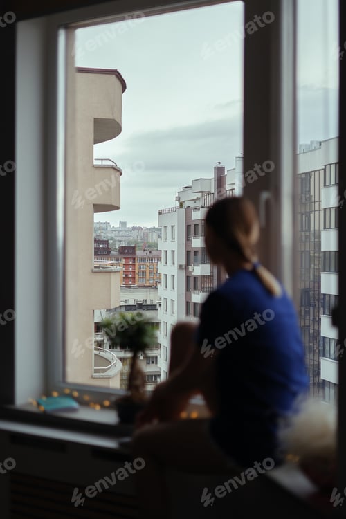 Preview: Young woman looking through window at the city
