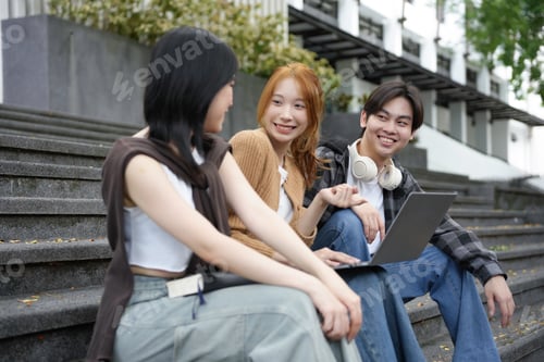 Preview: Three youths happily collaborate on a project outdoors, seated on steps and working on a laptop