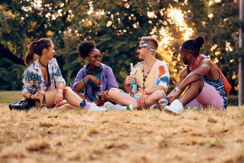 Preview: Happy friends talking while relaxing on a grass before open air concert.