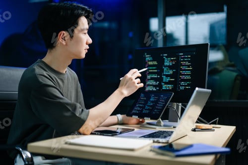 Preview: Young male programmer working with tablet and screen displaying code. Modern tech office setup,