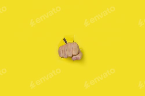 Preview: Fist punch through yellow paper background. Concept of aggression, punch, break, protest.