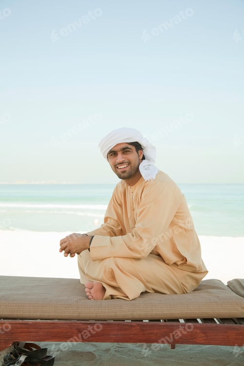Preview: Smiling man in traditional attire sitting by the beach