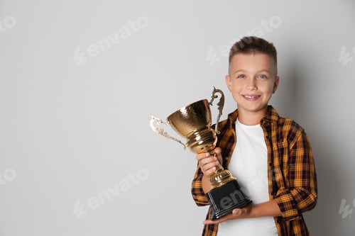 Preview: Happy boy with golden winning cup on light background. Space for text