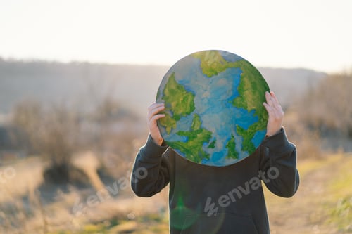 Preview: Little boy holding planet in hands against green spring background. Earth day