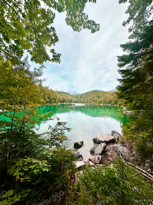 Preview: View Through Trees Branches To Green Blue Lake Eibsee in Germany On Forest Background, Blue Sky