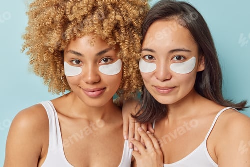 Preview: Photo of two mixed race young women stand closely to each other apply white patches under eyes under