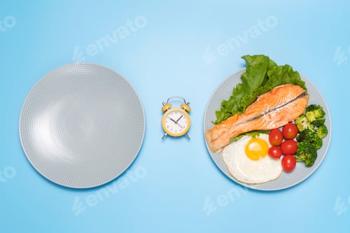 Preview: Plates empty and with food and an alarm clock on blue background, concept of intermittent fasting.