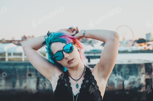Preview: Young female with tattoos and pink and blue hair playing with her hair posing in an amusement park