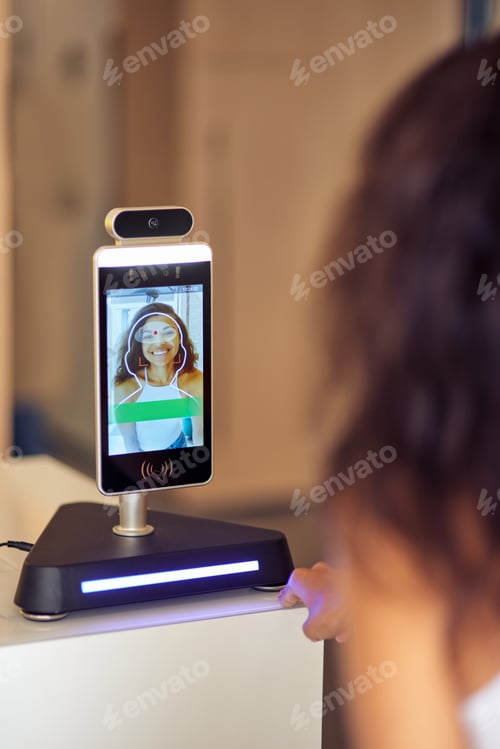 Preview: Rear view of female office worker using face recognition at work, business and identification