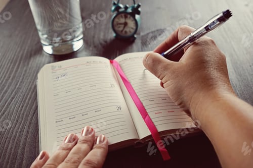 Preview: A woman's hand writes in her diary on the wooden table. Time to start concept