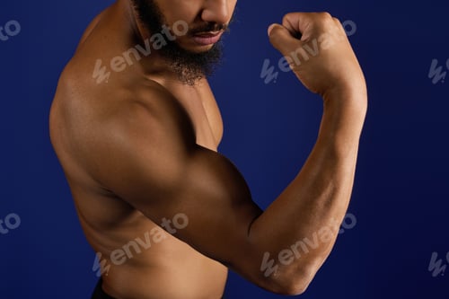 Preview: Athletic Black man flexing muscles against a bright blue backdrop while working out