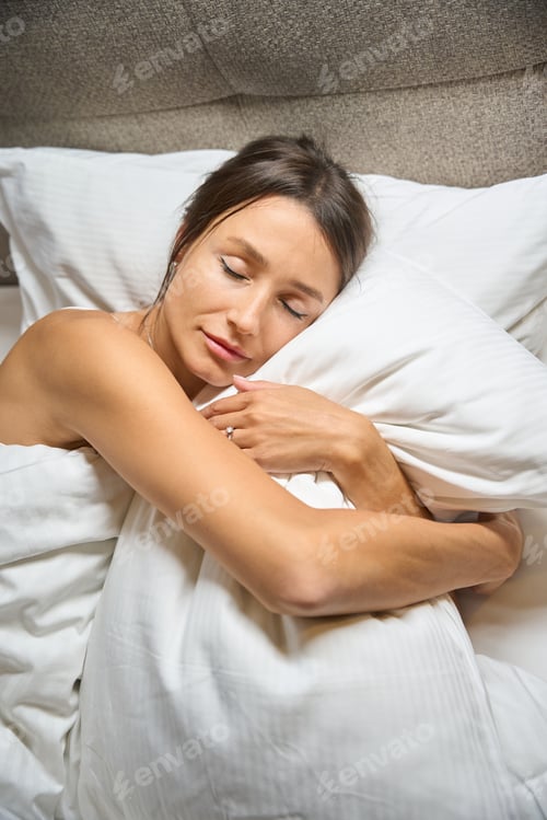 Preview: Top view of attractive caucasian woman hugging pillow while sleeping on bed