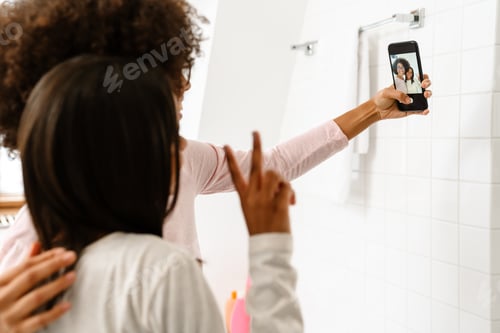 Preview: Black girl and her mother taking selfie on cellphone in bathroom