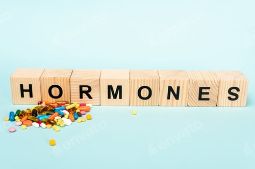 Preview: Wooden blocks with hormones lettering and pile of pills on blue background