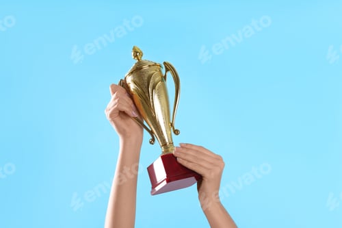 Preview: Woman holding gold trophy cup on light blue background, closeup