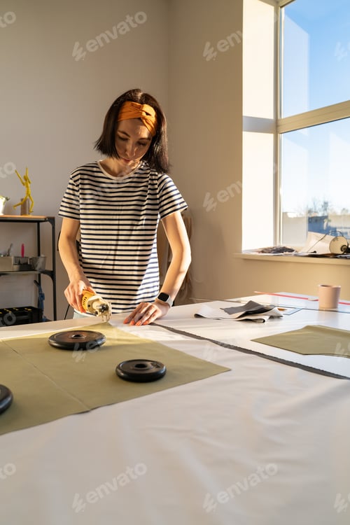 Preview: Cutting and sewing in tailor studio: sewer young woman work with fabric in design workshop studio