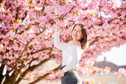 Preview: Woman allergic enjoying after treatment from seasonal allergy in front of blossom tree at spring.