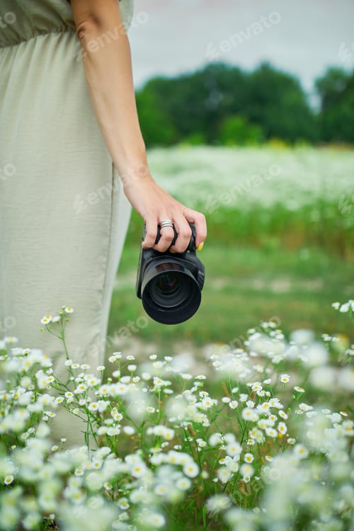 Preview: Unrecognizable woman hold digital camera in her hands on flower field landscape