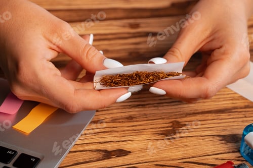 Preview: Close up of woman making hand rolled cigarette at wooden table