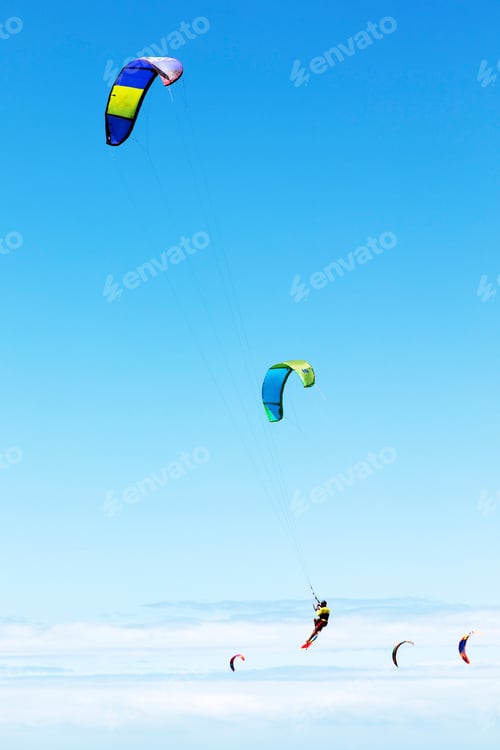 Preview: Kite surfers glide across a mirrorlike surface under a clear blue sky.