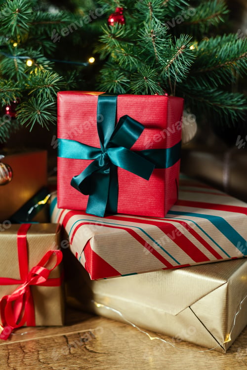 Preview: Stack of gifts in the lights of a garland under the Christmas tree.
