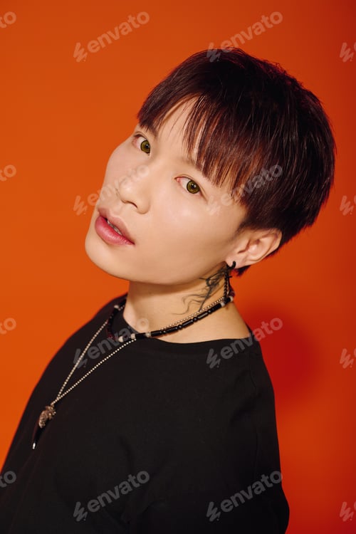 Preview: Stylish young man poses confidently against a bold orange background in a trendy outfit