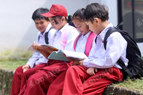 Preview: School kids in uniform sitting in a row and reading book together.