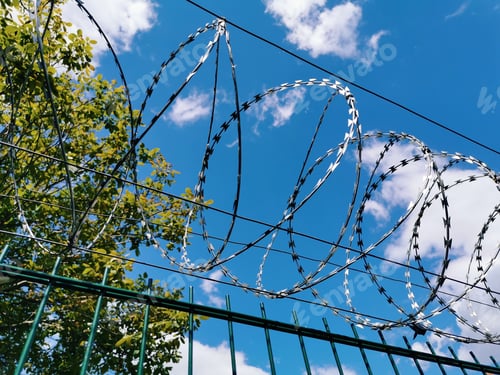 Preview: Low angle view of barbed wire fence against blue sky.
