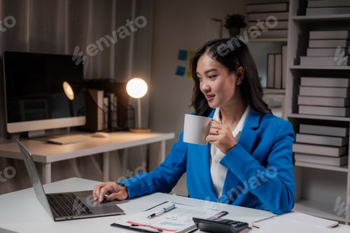 Preview: Asian businesswoman drinking coffee while working at night