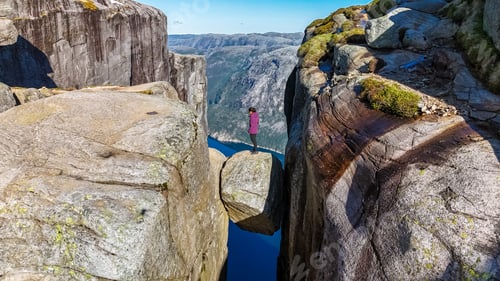 Preview: A lone hiker stands on the edge of the iconic Kjeragbolten cliff in Norway, gazing out at the