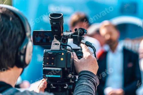 Preview: Cameraman At An Outdoor Media Event. Blurred Speaker In The Back