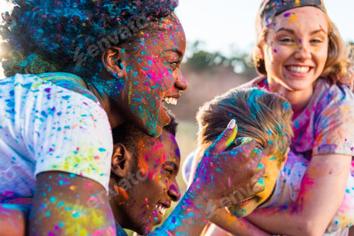 Preview: happy young multiethnic couples with colorful paint on clothes piggybacking at holi festival