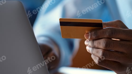 Preview: Serious man pays online holding credit card and typing on white laptop